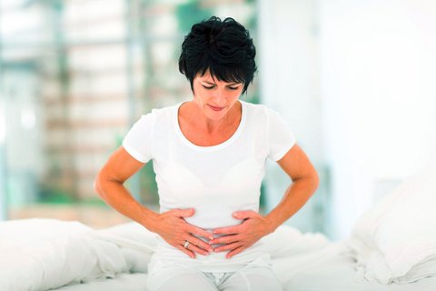Frau sitzt mit Bauchschmerzen